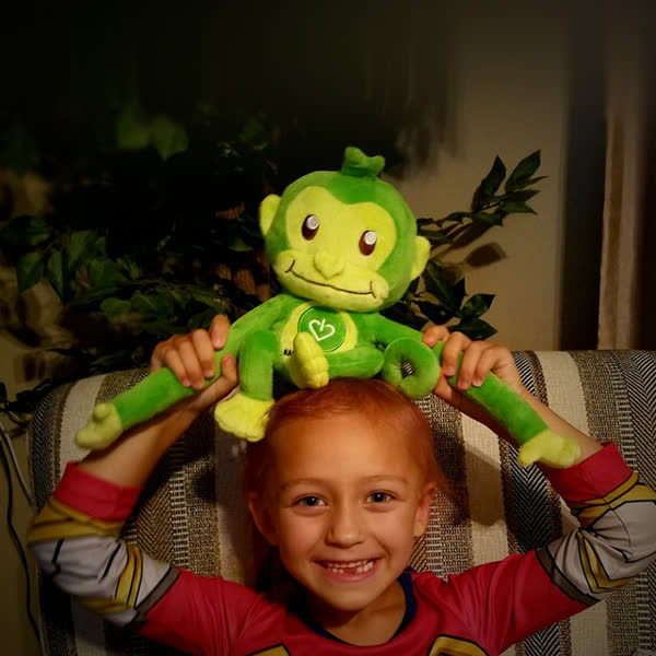 A beaming young patient holding Hope, GameChanger's green monkey, above their head.