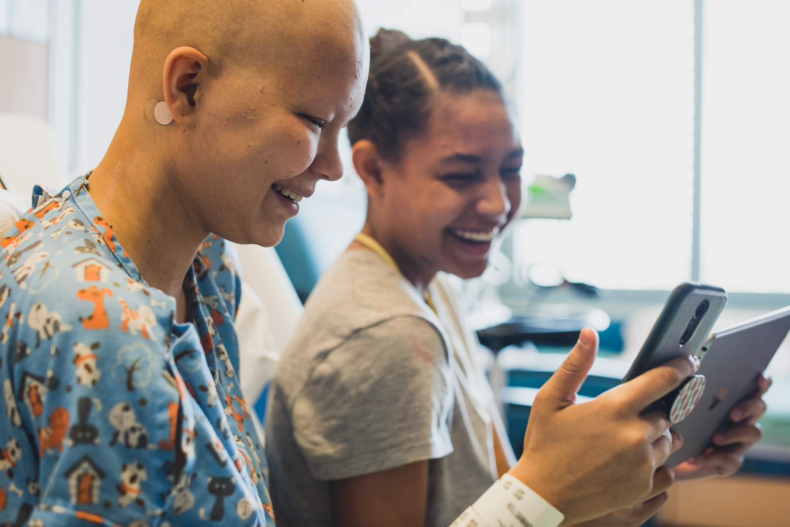 Two young patients laughing together over a tablet in the hospital.